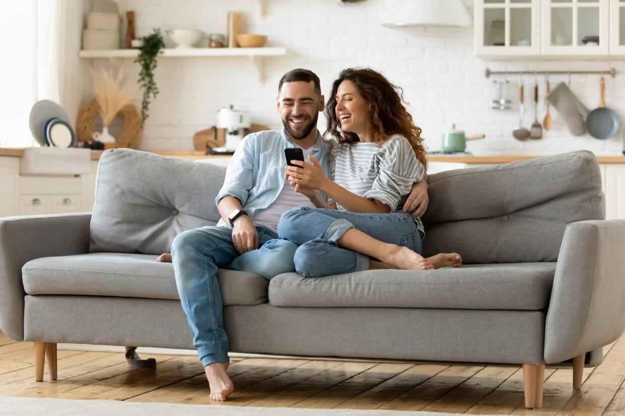 Happy,Young,Woman,And,Man,Hugging,,Using,Smartphone,Together,,Sitting